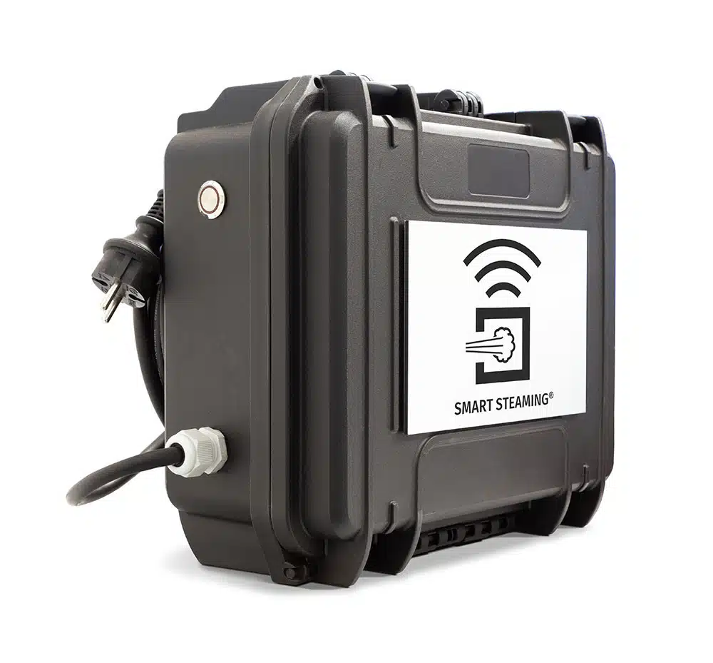 Ein kompakter, schwarzer Hartschalenkoffer mit Tragegriff ist abgebildet. An der Seite ist ein Stromkabel angeschlossen. Auf der Front befindet sich ein Schild mit einem stilisierten Sensor- oder WLAN-Symbol und der Aufschrift "SMART STEAMING". 